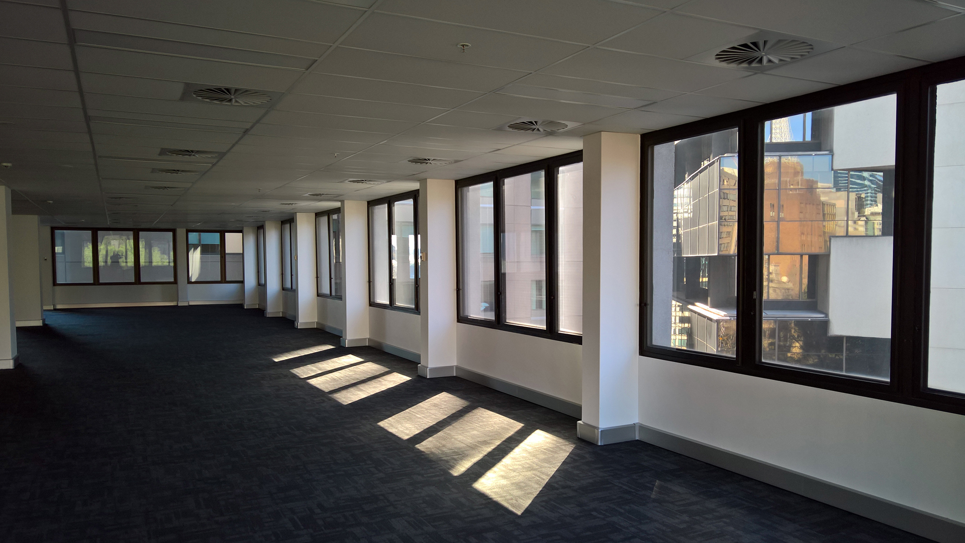 Vacant commercial office floor with natural daylight and city views through large windows.