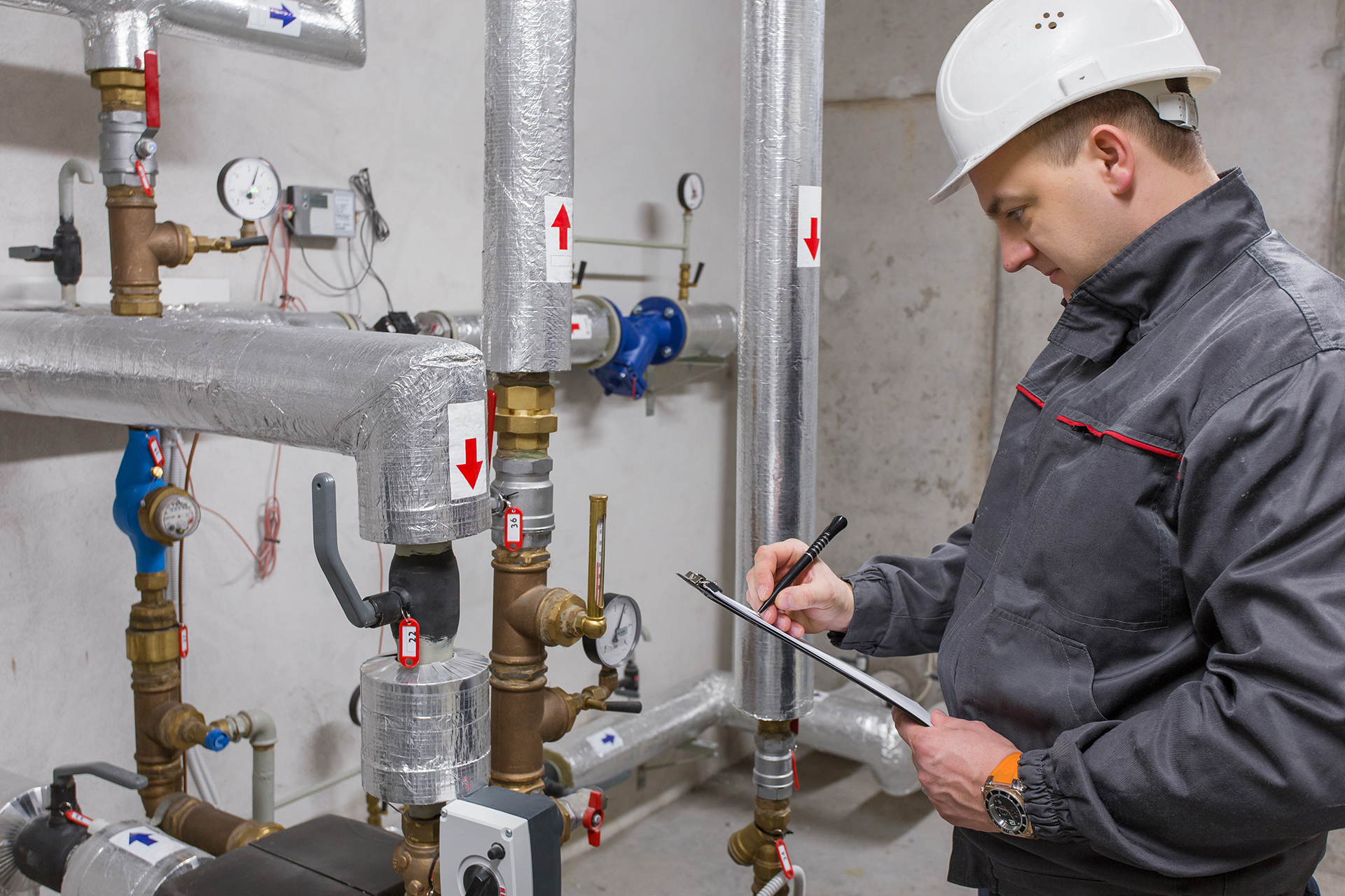 Building services technician inspecting mechanical plant equipment and recording maintenance data for governance and compliance purposes.