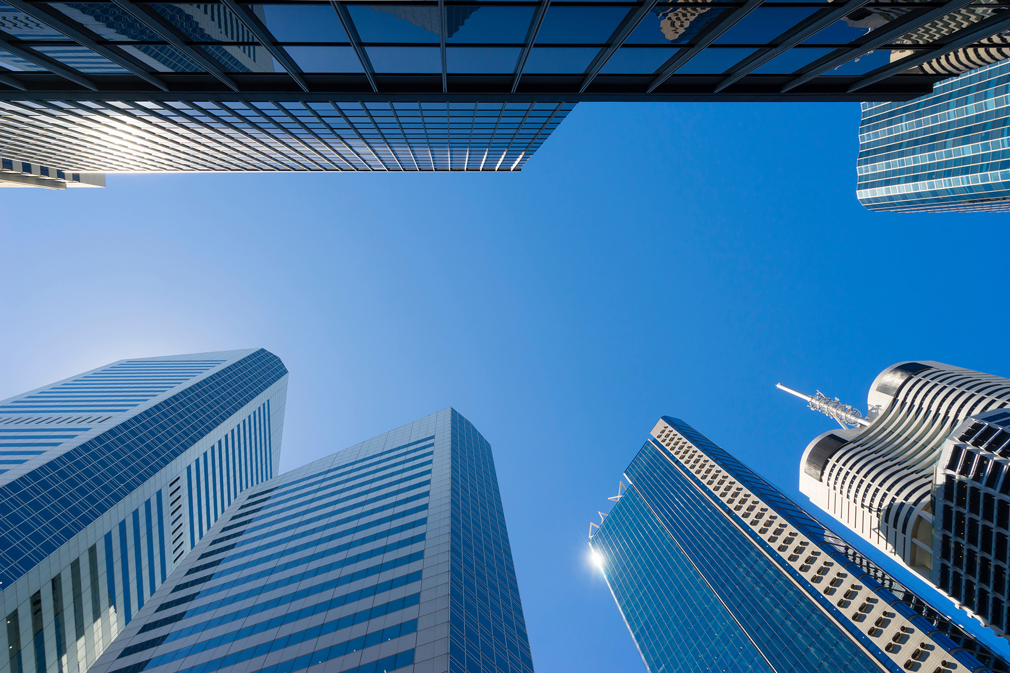 Modern commercial office towers viewed from street level looking upward into a blue sky.