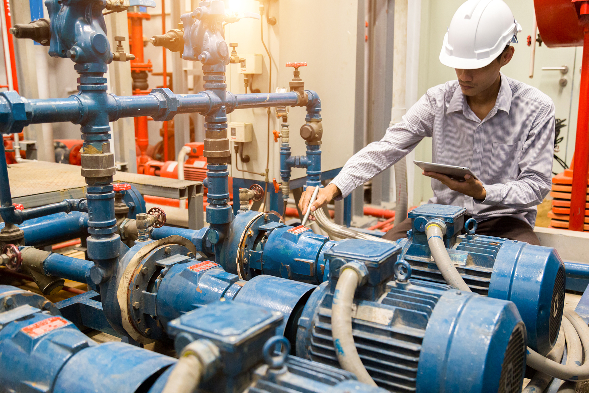 Contractor inspecting building plant equipment with a tablet as part of strata contractor management and maintenance oversight.