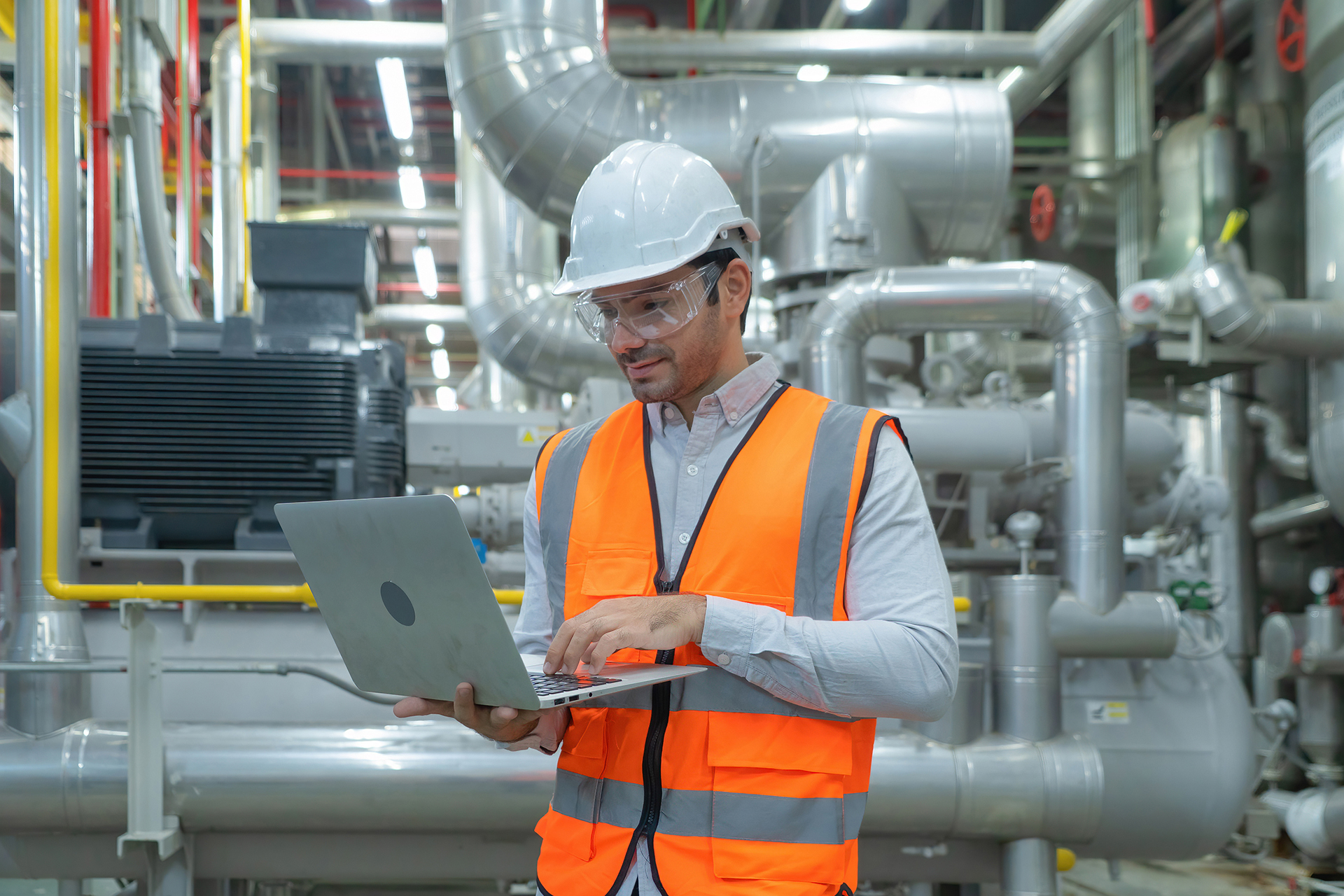 Facility manager using a laptop in a commercial plant room representing governance, risk management, and operational oversight.